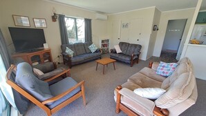 Una sala de estar con sofá, sillones, una mesa de centro, televisor y estantería.
