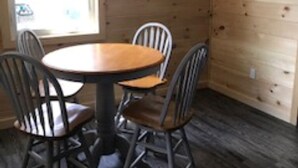 Ein Zimmer mit Holzvertäfelung, einem runden Tisch und vier Stühlen. Eine Uhr ist an der Wand befestigt, und ein gerahmtes Schild zeigt den Schriftzug "Our Place."