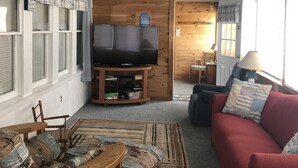 Ein gemütliches Wohnzimmer mit Holzboden, einem roten Sofa, einem Couchtisch aus Holz und einer TV-Konsole mit einem Flachbildfernseher.