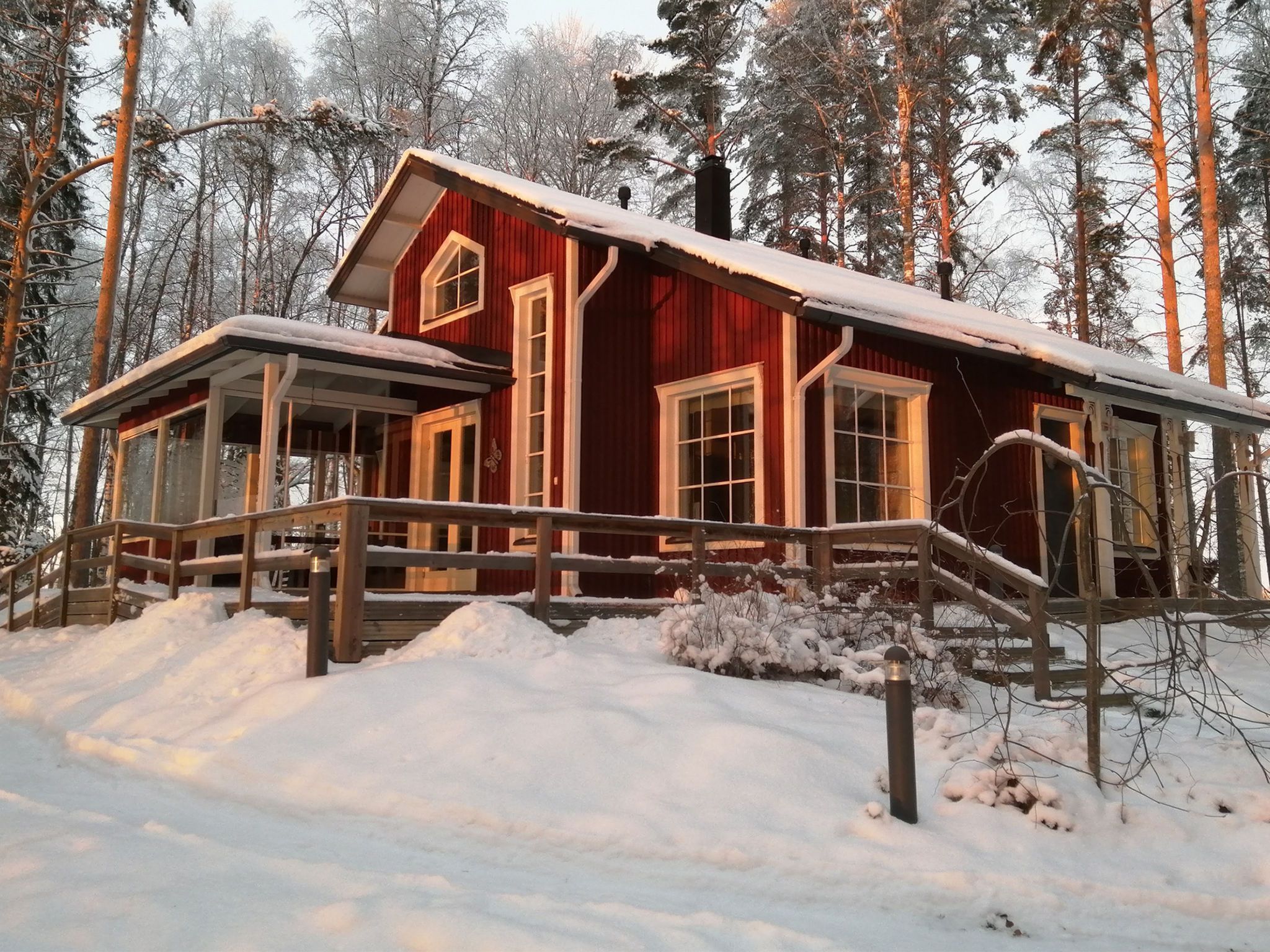Une cabane rouge avec une terrasse en bois, entourée d’arbres couverts de neige.