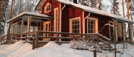 Una cabaña roja con terraza de madera, rodeada de árboles cubiertos de nieve.