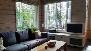 A cozy living room with a sofa, a coffee table, a TV, and large windows offering a view of greenery. - Villa raita by Interhome (Rääkkylä)
