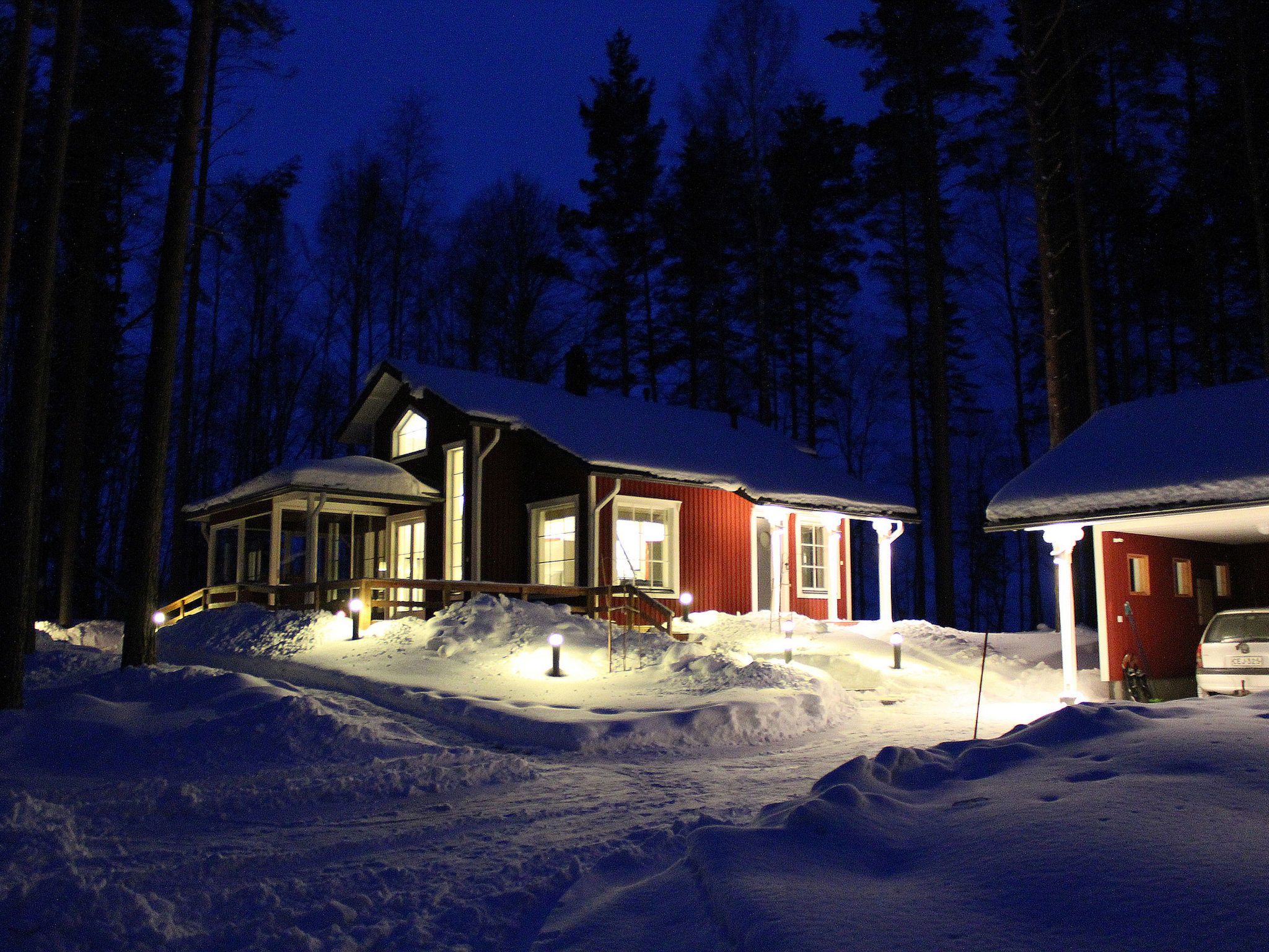 Una casa cubierta de nieve con porche y garaje, rodeada de árboles.