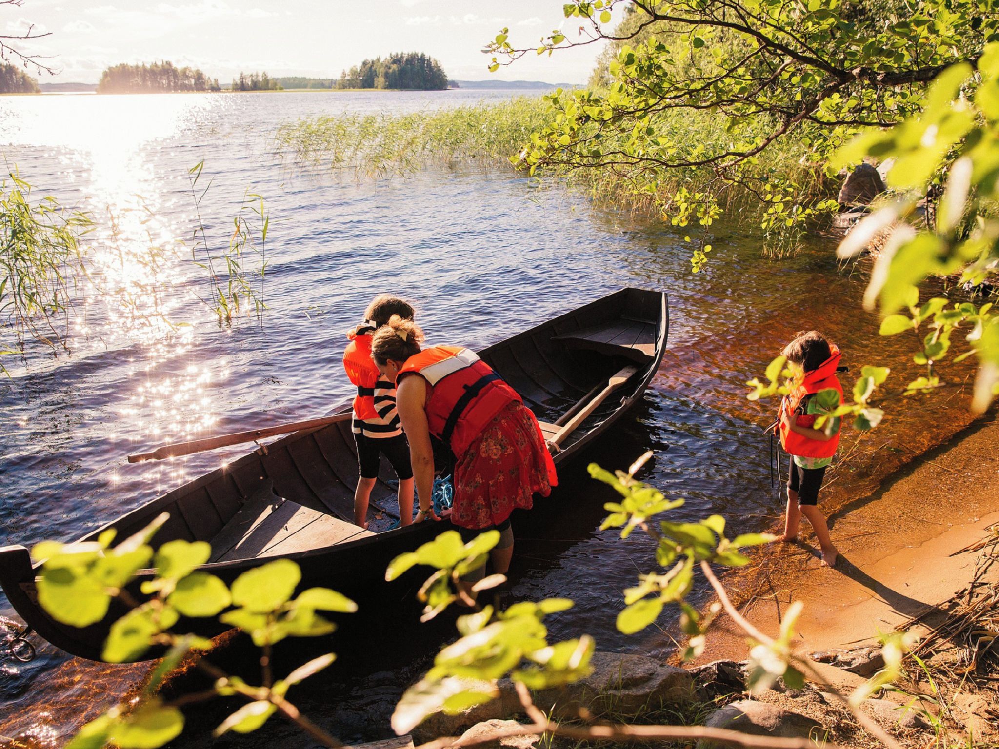 A wooden canoe on a calm river with people wearing life jackets.