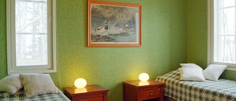 A bedroom with two beds, a nightstand with a lamp, a framed picture on the wall, and a window.