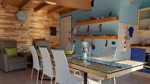 A dining area with a glass-top table, white chairs, a wooden ceiling, and a blue wall with shelves. - Ca 'De' Mumi, New Opening Old Town from 5 Apr '19 (Luino)