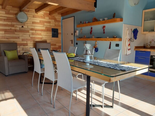 A dining area with a glass-top table, white chairs, a wooden ceiling, and a blue wall with shelves. - Ca 'De' Mumi, New Opening Old Town from 5 Apr '19 (Luino)