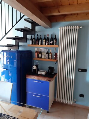 Una cucina con un frigorifero blu, scaffali in legno con bottiglie di vino, un bollitore e una macchina per il caffè.
