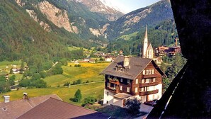 Ein Bergdorf mit traditioneller Architektur, darunter ein markanter Kirchturm, umgeben von üppiger Vegetation und Bergen.