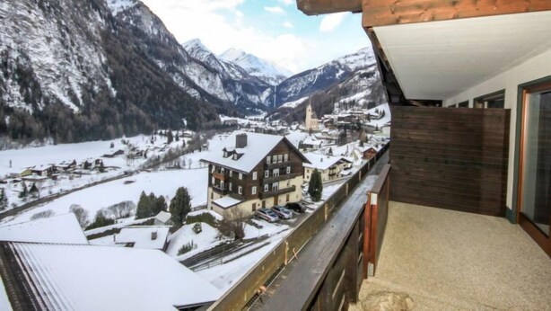 Ein Balkon mit Blick auf ein verschneites Dorf und Berge.