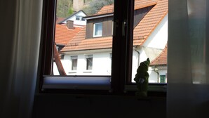 A window with a view of a castle on a hill, a white building with a red roof, and a stuffed toy on the windowsill. - Nice central apartment with S-Bahn connection to Heidelberg and castle view (Hirschhorn (Neckar))