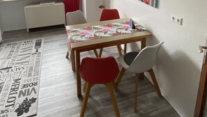 A dining area with a table, chairs, a window with curtains, a radiator, and a wall with a clock and a colorful painting. - Nice central apartment with S-Bahn connection to Heidelberg and castle view (Hirschhorn (Neckar))