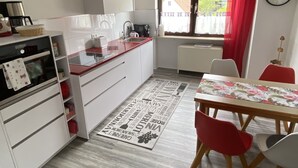A compact kitchen with white cabinets, a red countertop, and a dining area with a table and chairs. - Nice central apartment with S-Bahn connection to Heidelberg and castle view (Hirschhorn (Neckar))