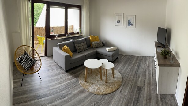 A modern living room with a grey sectional sofa, two white round tables, a yellow chair, and a TV on a wooden cabinet. - Nice central apartment with S-Bahn connection to Heidelberg and castle view (Hirschhorn (Neckar))