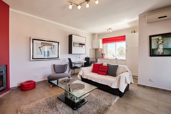 A modern living room with a glass coffee table, a sofa, and a dining area with a red accent wall.