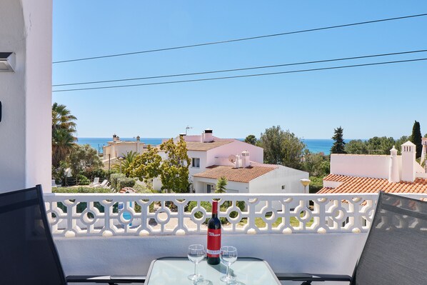 Ein Balkon mit Tisch für zwei Personen, Blick auf die Küste mit Gebäuden und dem Meer.