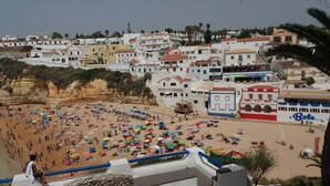 Eine Küstenstadt mit Strandabschnitt, der farbenfrohe Sonnenschirme und ein in der Nähe liegendes Boot namens 'Bote' zeigt.