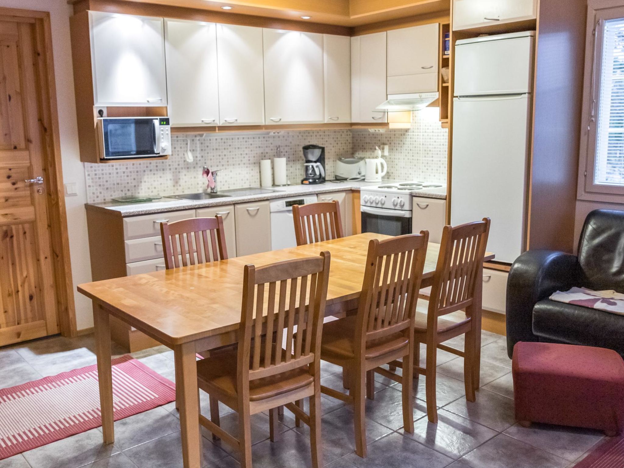A compact kitchen with white cabinets, a wooden dining table, and four chairs.