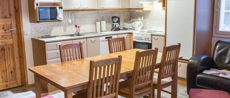 A compact kitchen with white cabinets, a wooden dining table, and four chairs.