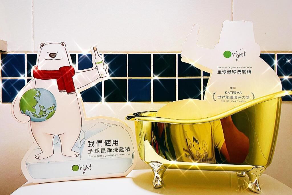 A polar bear holding a globe and a bottle of shampoo, with a golden bathtub and a mirror reflecting a person.
