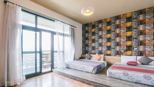 A hotel room with two beds, a large window with curtains, a view of the sea, and a patterned wall. - Time B&B (Hengchun)