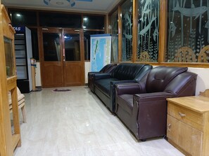 A room with a wooden cabinet, a leather sofa, a wooden table, and a map on the wall. - Blue Ocean Resort (Port Blair)
