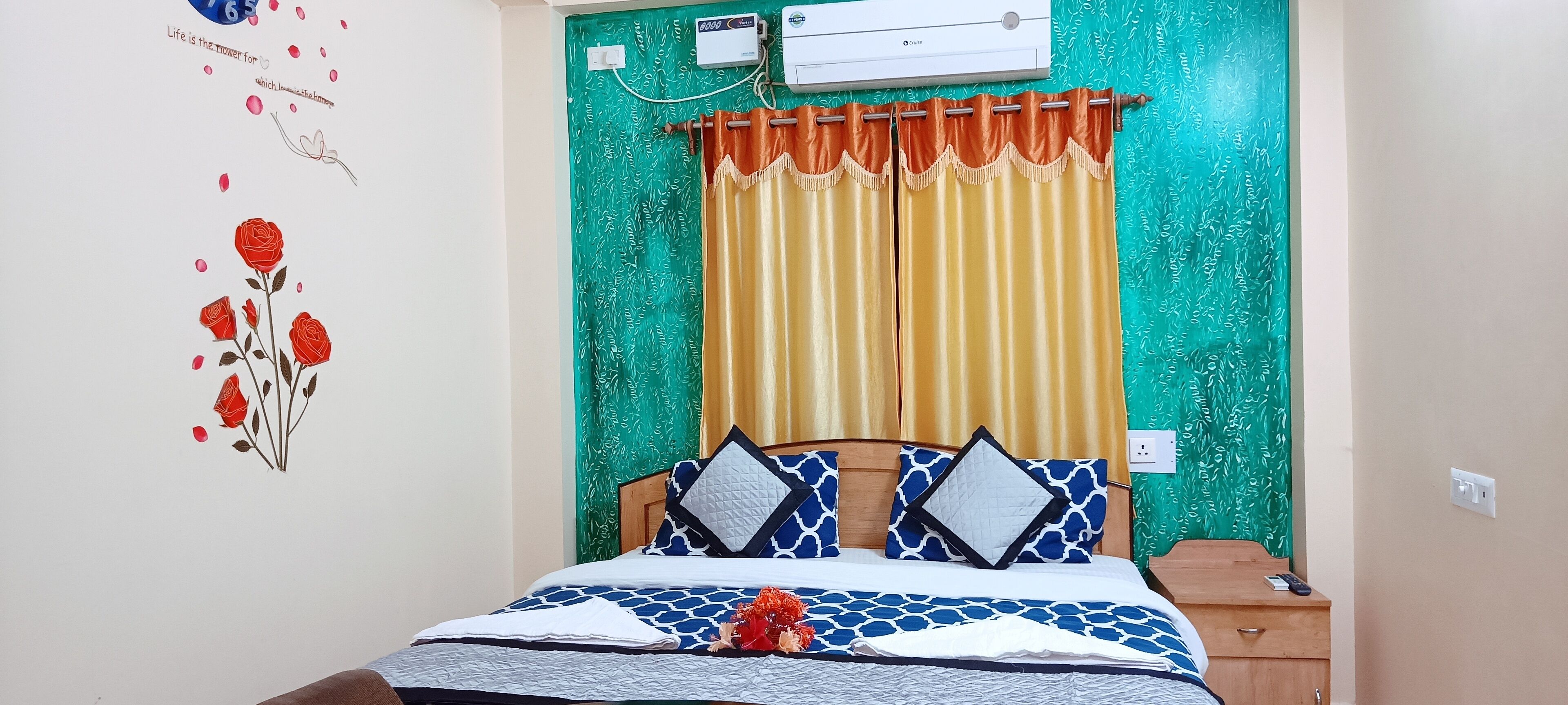 A bedroom with a bed, a nightstand, a wall-mounted air conditioner, and a green patterned curtain.