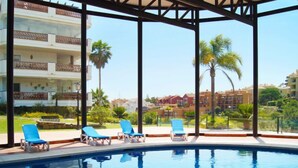 A swimming pool with blue lounge chairs and a view of a residential area with palm trees and buildings. - Island of Riviera Golf by Interhome (Mijas Costa)