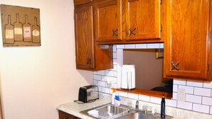 A kitchen with wooden cabinets, a double sink, a toaster, and a wine bottle decoration on the wall.