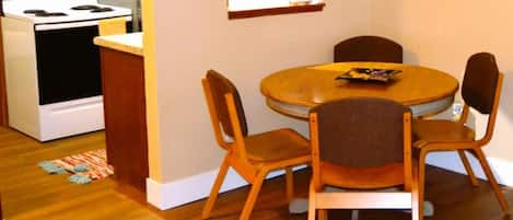 Una cocina compacta con estufa, horno y muebles de madera. Hay una mesa de comedor con cuatro sillas y una pequeña alfombra en el suelo.