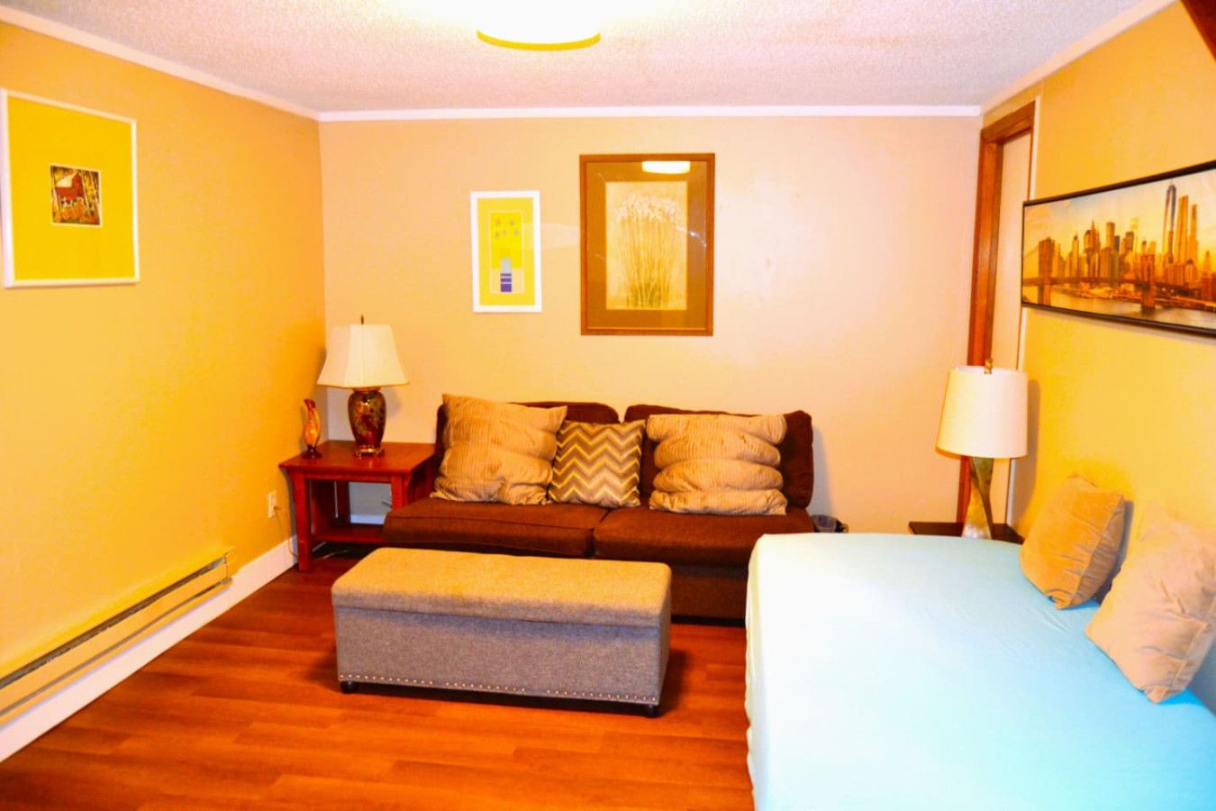 A room with a sofa, a bed, a small table, and a lamp.
