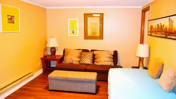 A room with a sofa, a bed, a small table, and a lamp.