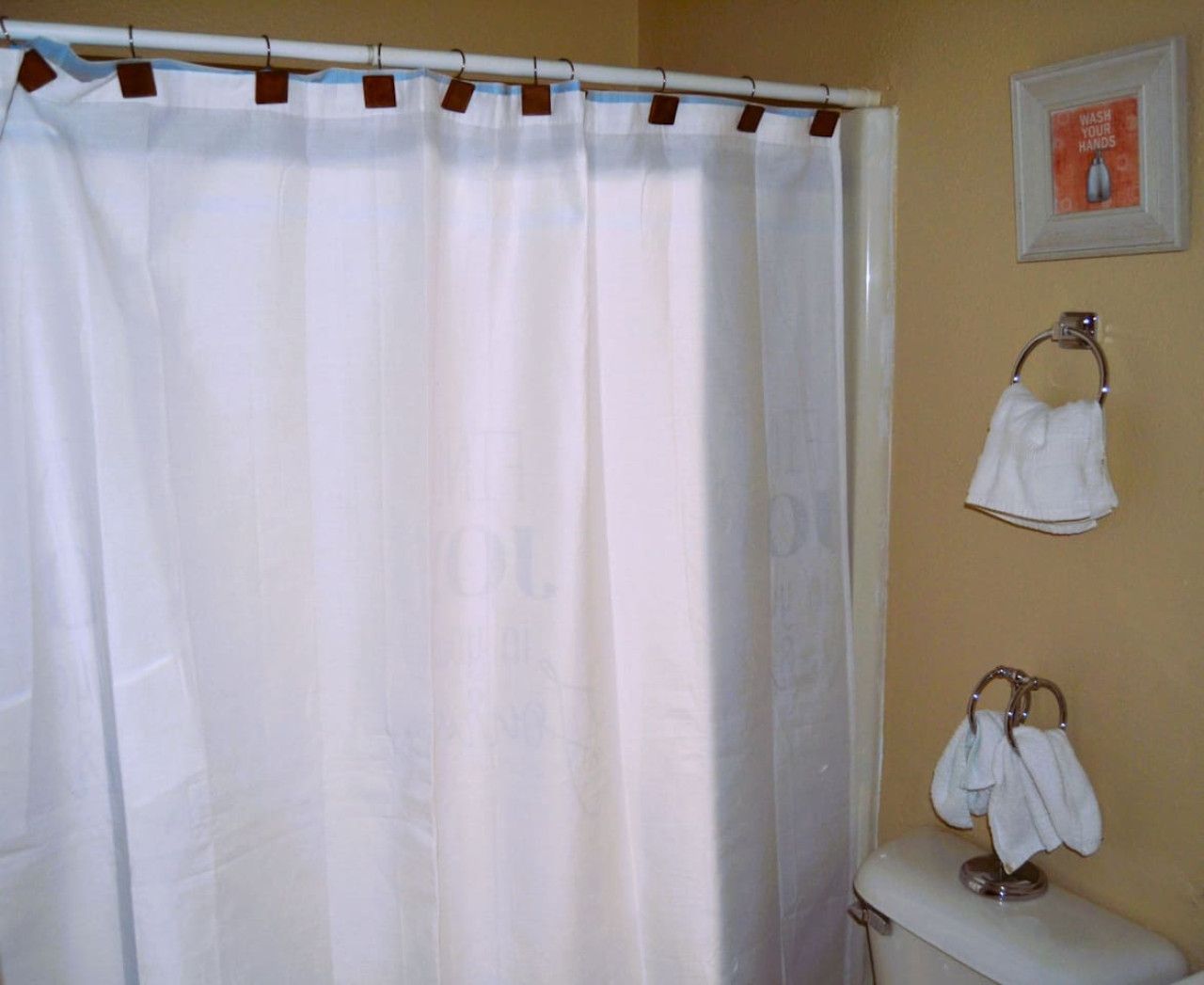 Een badkamer met een witte douchegordijn, een toilet en twee handdoeken aan haken.