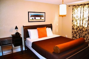 Habitación de hotel con cama, mesita de noche, lámpara, un cuadro en la pared y ventana con cortinas.
