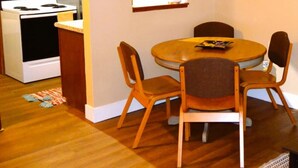 A compact kitchen with a stove, oven, and wooden cabinets. There is a dining table with four chairs and a small rug on the floor.