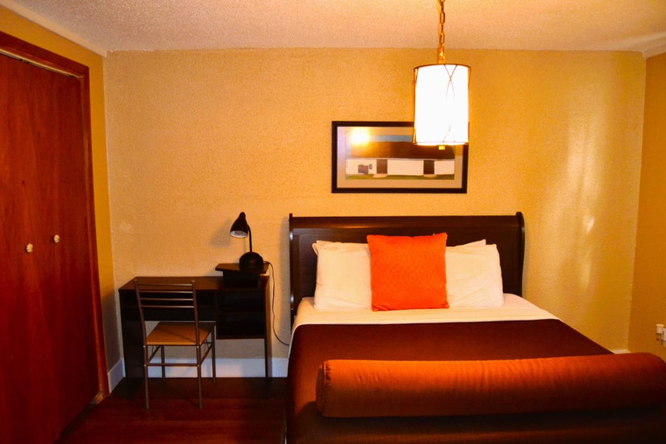 A hotel room with a bed, a desk, a chair, and a lamp.