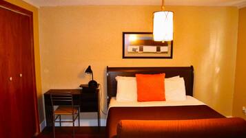 A hotel room with a bed, a desk, a chair, and a lamp.