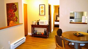 A dining area with a round wooden table and chairs, a small side table with a microwave, and a hallway leading to a kitchen.