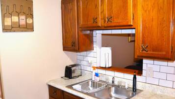 A kitchen with wooden cabinets, a double sink, a toaster, and a wine bottle decoration on the wall.