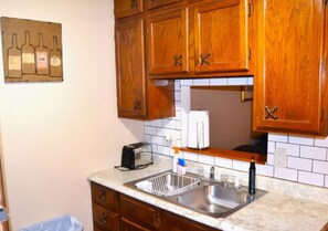Una cocina con armarios de madera, un lavamanos doble, un tostador y una decoración con una botella de vino en la pared.
