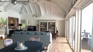 Een ruime woonkamer met een hoge plafond, een kroonluchter, een grote bank, een eettafel met stoelen en een boekenplank vol boeken.