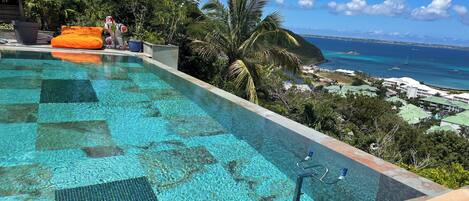A clear blue infinity pool with a view of the ocean and a tropical landscape.