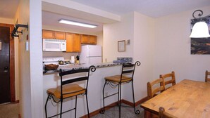 Uma cozinha com armários de madeira, micro-ondas, geladeira e um espaço de jantar com mesa de madeira e cadeiras de metal.