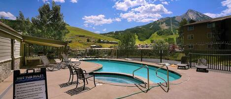 A hot tub area with a sign listing rules, surrounded by lounge chairs and a pool.