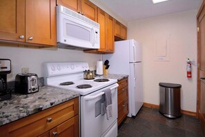 A compact kitchen with wooden cabinets, a white stove, a microwave, and a refrigerator. - Silvery Lupine, Hot tub, pool, shuttle (Crested Butte)