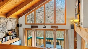A wooden interior with a stone fireplace, large windows, and a balcony. - Summer Retreat - Treetop View Cabin with Hot tub & Pool Table (Gatlinburg)