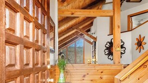 A wooden interior with a large wooden door, a staircase, and a small table with a vase. - Summer Retreat - Treetop View Cabin with Hot tub & Pool Table (Gatlinburg)
