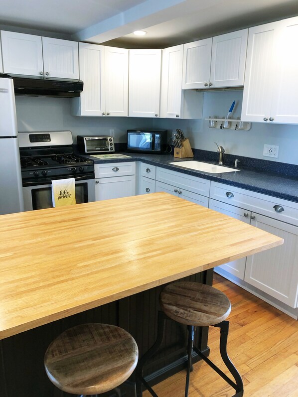 A modern kitchen with white cabinets, a wooden countertop, a stove, a microwave, and two stools.