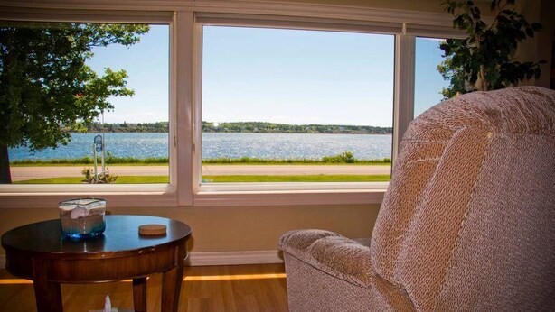 A room with a view of a lake through large windows, a round wooden table with a candle, and a textured armchair. - Waterfront Vacation Home-4 bedrooms-2.5bath-Laundry room inside-2 heat pumps (York)