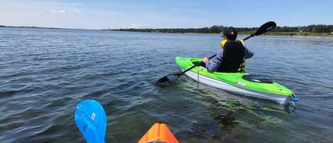 Two kayaks on calm water, one green and one orange, with a person paddling the green kayak.